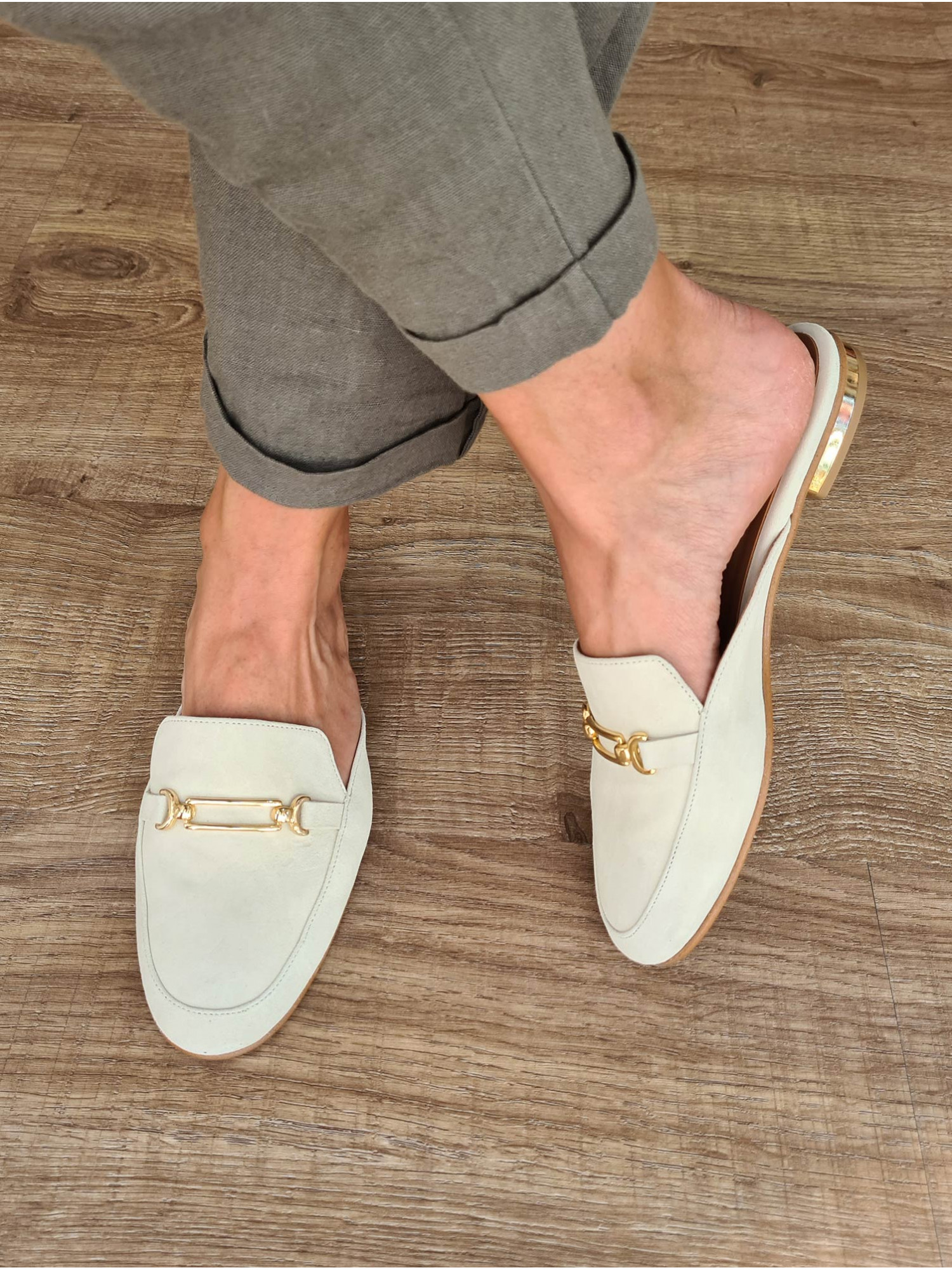 Zapato mocasín plano destalonado. Fabricado en España en piel de ante color beige y detalle de cadena dorada.